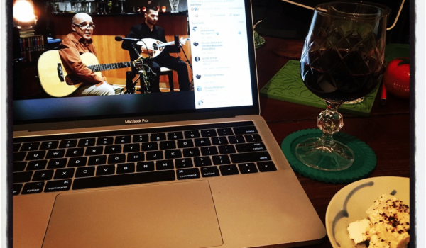 A laptop showing two musicians performing on Facebook Live sits next to food and drink due to COVID-19.