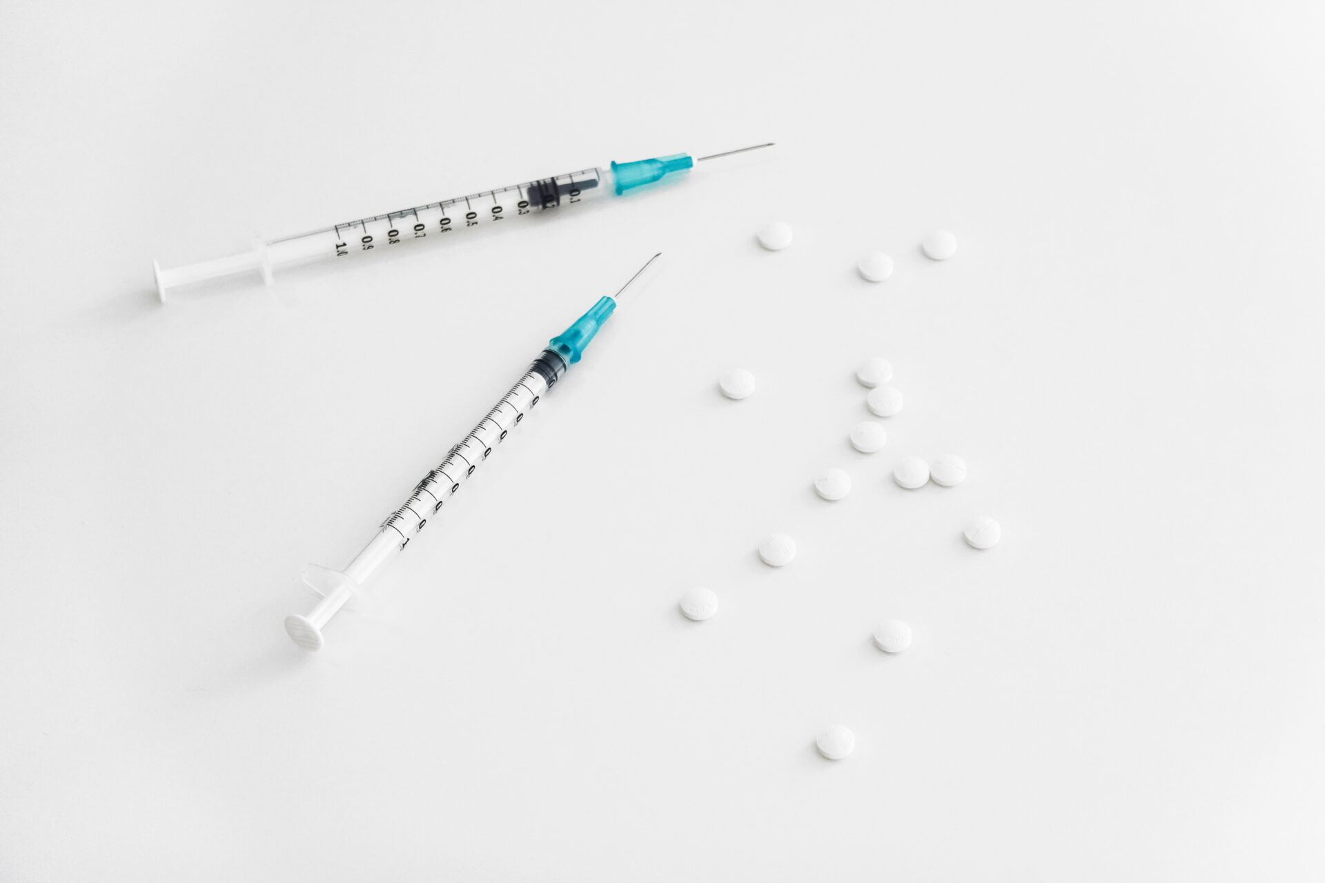 White pills and two syringes scattered on a white table.