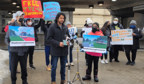 A group of people holdinh up several colourful signs as they stand outside in front of a subway street entrance.