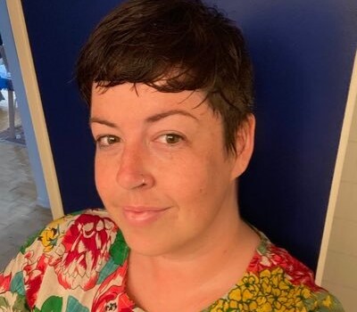 A person with brown hair wearing a red and green floral shirt.