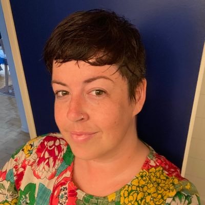 A person with brown hair wearing a red and green floral shirt.
